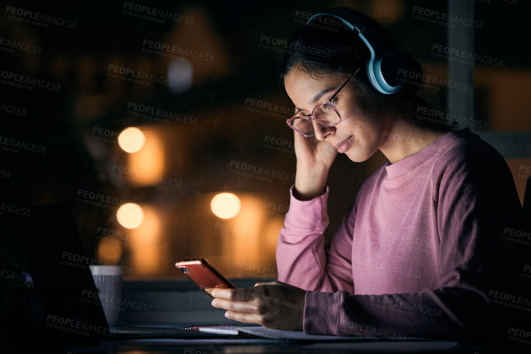 Buy stock photo Networking, night and woman on a cellphone with headphones while listening to music, radio or podcast. Happy, smile and girl browsing social media, mobile app or internet with phone at a desk at home