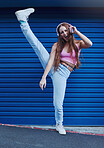 Music, freedom and excited girl on blue background in city listening to track, audio and radio with headphones. Freedom, lifestyle and woman with leg up for dance, happy attitude and streaming song