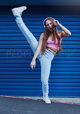 Buy stock photo Crazy music, freedom and excited girl on blue background in city listening to track and audio on headphones. Fashion, lifestyle and woman with leg up for dance, happy attitude or streaming song