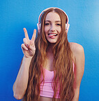 Music, peace and tongue with the portrait of a woman on a blue background while listening to the radio. Face, hand and headphones with an attractive young female streaming an audio playlist or song