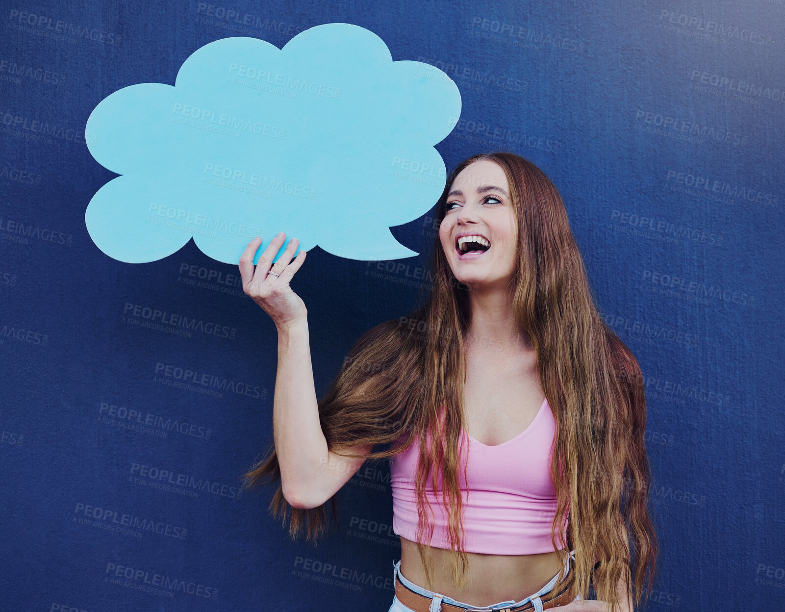 Buy stock photo Happy woman holding a speech bubble with mockup space standing by a blue wall with a sign. Gen z, happiness and young female with a chat board with mock up or copy space for marketing or advertising.