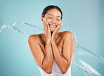 Water, splash and woman in a studio for a skincare, beauty and natural cosmetic face routine. Health, wellness and female model with a fresh organic facial treatment isolated by a blue background.