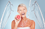 Woman, grapefruit and studio portrait with water splash, happiness and cosmetics for wellness by blue background. Senior model, citrus fruit and vitamin c for health, nutrition and self care process