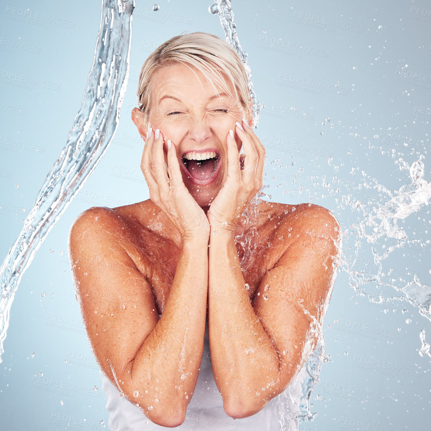 Buy stock photo Skincare, excited and portrait of a woman with a water splash isolated on a blue background. Self care, happy and face of an elderly beauty model cleaning her body for wellness on a studio backdrop