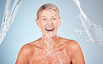 Skincare, senior and portrait of a woman with a water splash isolated on a blue background. Self care, happy and face of an excited elderly model cleaning her body for wellness on a studio backdrop