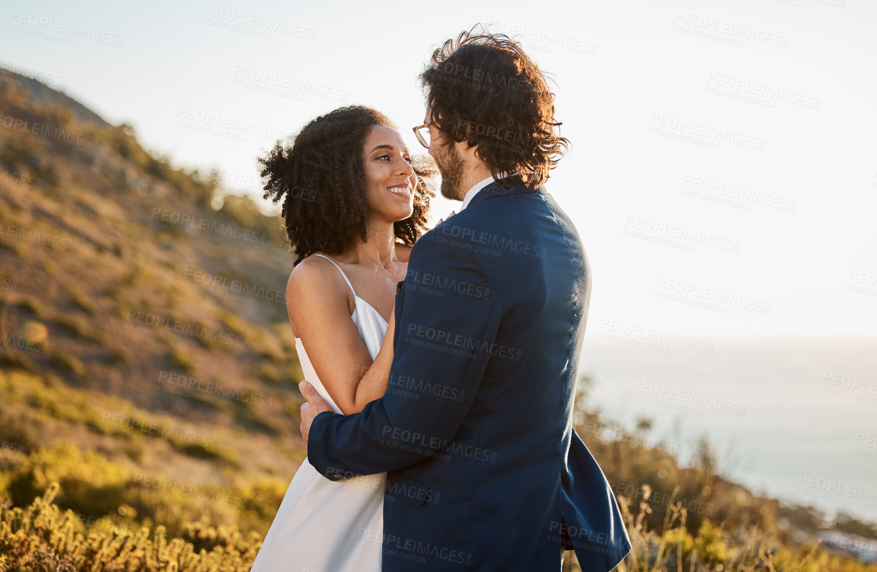 Buy stock photo Marriage, love and bride with groom on mountain for wedding ceremony, commitment and celebration. Romance, happiness and interracial couple bonding, hug and smile with ocean, nature and outdoors