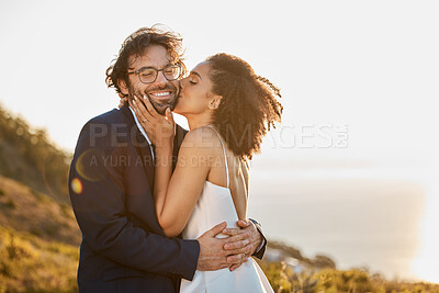 Buy stock photo Kiss, hug and wedding bride with groom for love, care and connection together in nature. Happy, partner and bond of interracial people at outdoor marriage celebration on hill in sunset.