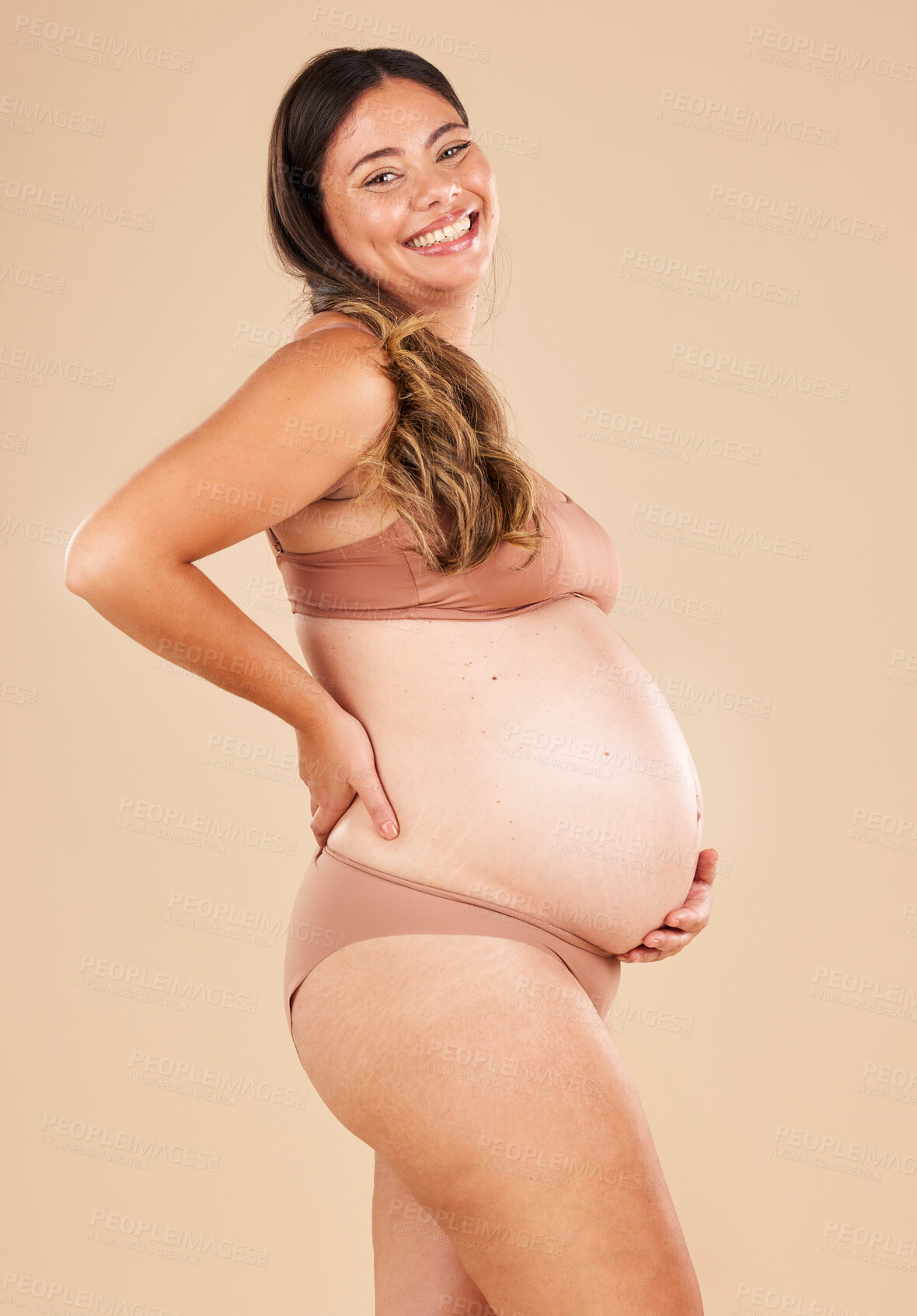 Buy stock photo Portrait, pregnant and stomach with a model woman in studio on a beige background for motherhood. Baby, beauty and wellness with an attractive young mother in underwear for pregnancy or body health