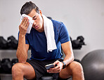 Sweat, tired and man resting in the gym after a intense workout, exercise sports training. Fitness, sport and male athlete networking on social media with a phone after exercising in wellness studio.