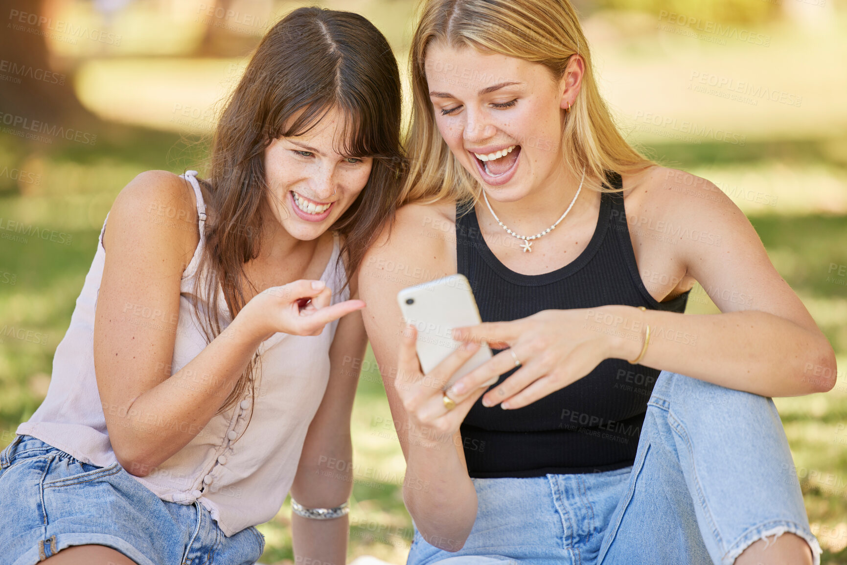 Buy stock photo Happy, park and phone with a couple of friends online together for funny comic social media post. Women outdoor on grass with smartphone for communication, 5g connection and typing search on internet