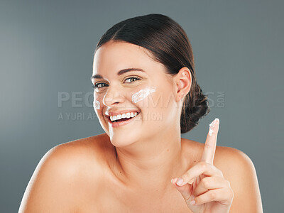 Buy stock photo Portrait, skincare and woman with cream, cosmetics and smile with girl on grey studio background. Face, female and happy lady with lotion, creme and dermatology for treatment and grooming routine