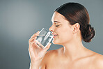 Woman, glass and drinking water for hydration, skincare or nutrition for sustainability against grey studio background. Happy female with smile in beauty for fresh clean sustainable liquid on mockup