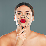 Beauty, magnifying glass and portrait of a woman in studio with a makeup, skincare and natural routine. Face, cosmetic and female model with glass lens on her mouth while isolated by gray background.