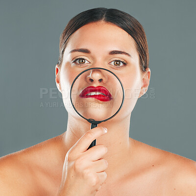 Buy stock photo Portrait, magnifying glass and lips with a model woman in studio on a gray background for red makeup. Face, cosmetics or search with an attractive and funny young female checking her skin