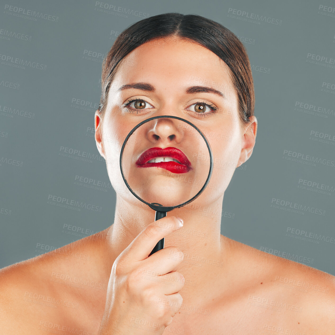 Buy stock photo Portrait, magnifying glass and lips with a model woman in studio on a gray background for red makeup. Face, cosmetics or search with an attractive and funny young female checking her skin