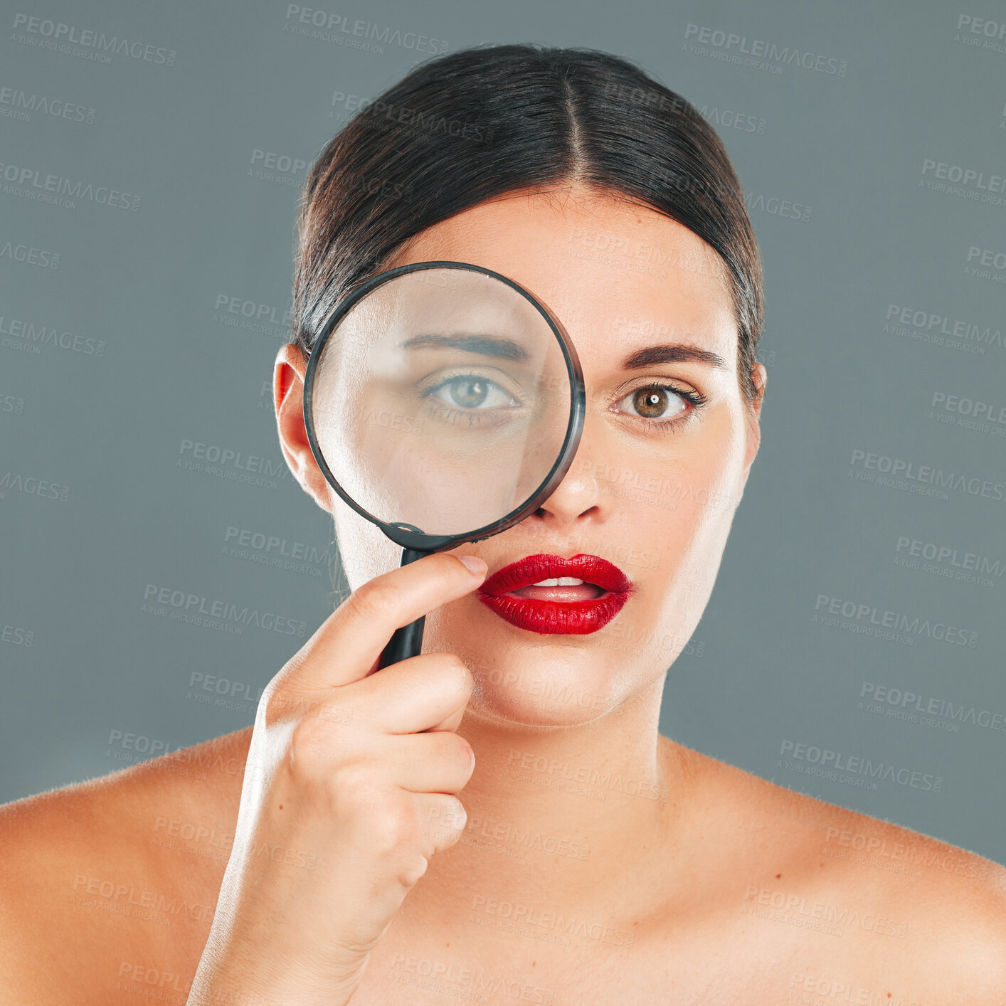 Buy stock photo Portrait, magnifying glass and eye with a model woman in studio on a gray background for beauty or skincare. Face, makeup and search with an attractive young woman checking her skin for cleaning
