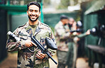 Paintball, gun and portrait of a man soldier in a camouflage military outfit for extreme sports. Happy, smile and male player in army clothes with a pistol preparing for a match in an outdoor arena.