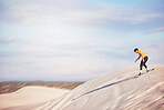 Sandboard, desert and mockup with a sports man outdoor on the sand dunes for recreation, fun or adventure. Sky, nature and mock up with a male athlete or sandboarding moving downhill at speed 