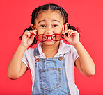 Eyes, glasses in hands and portrait of child with cute smile and isolated on red background. Vision, eyesight and happy playful expression, goofy little girl holding spectacles for eyesight in studio