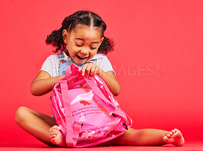Buy stock photo School, bag and red background with a student black girl in studio sitting on the floor against a wall. Children, education and excited with a female kid pupil getting ready for learning, or growth