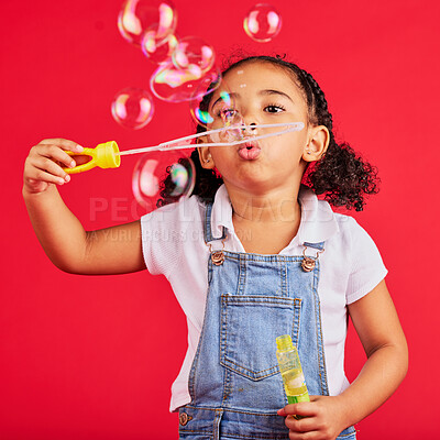 Buy stock photo Little girl, playing or blowing bubbles on isolated red background in hand eye coordination, activity or fun game. Child, kid or youth with soap, wand or toy in studio for breathing development skill