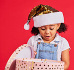 Christmas, gift and girl child surprise, wow and curious in studio, happy and shock against red background. Box, present and excited toddler express omg, cheer and happiness for festive celebration