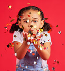 Young girl, kid blowing confetti with party and celebration, gold and glitter isolated against red background. Fun, youth and child at event, celebrate and birthday in studio with decoration