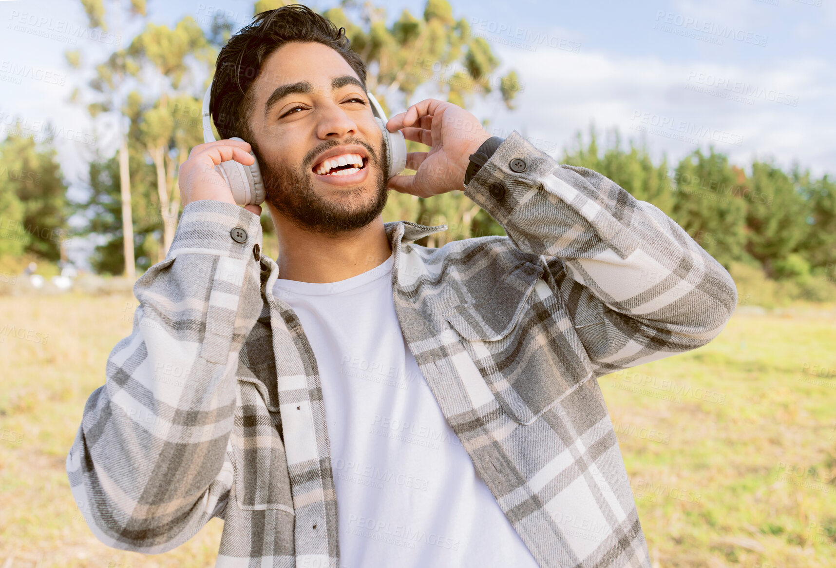 Buy stock photo Happy, man and music with headphones in forest, laugh and relax on blue sky, tree and space background. Radio, earphones and guy, smile and joy while listening to audio, podcast or track in nature