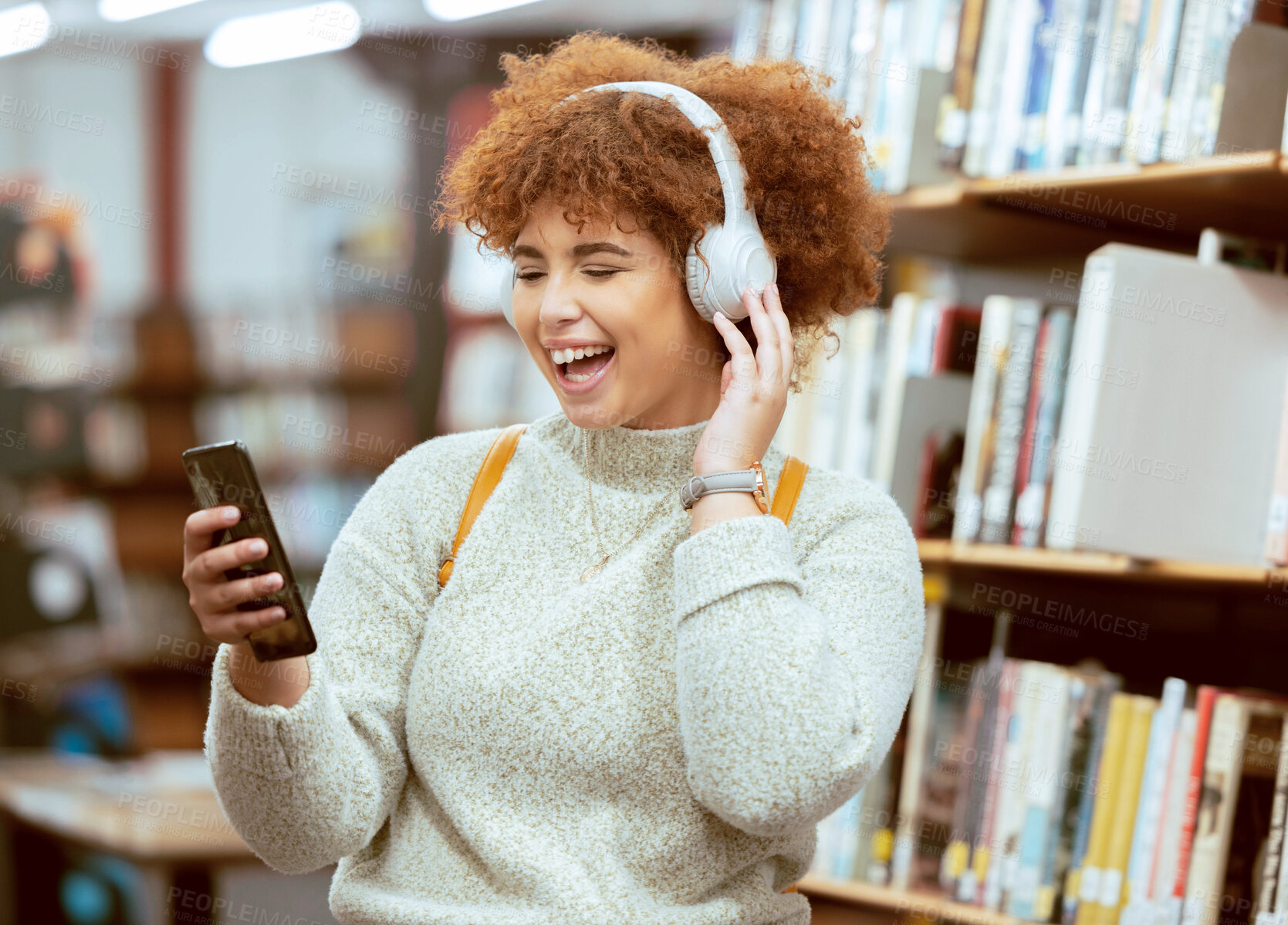 Buy stock photo Black woman, phone and music in library with headphones, streaming and laugh for meme on web app. University student, funny blog or social media with smile, smartphone and learning for education goal