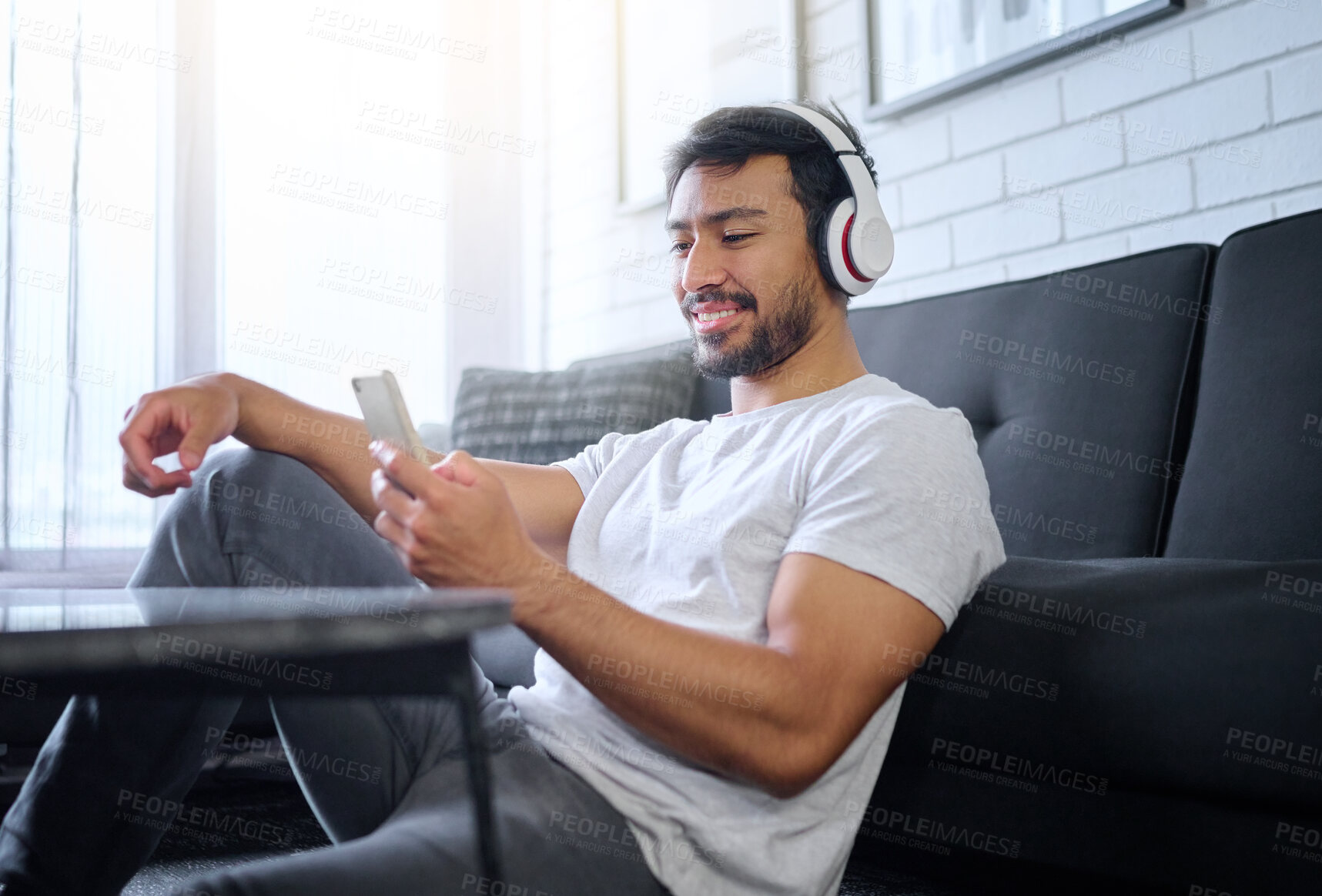 Buy stock photo Phone, music and man with headphones in home living room streaming radio or podcast. Cellphone, technology and male in lounge sitting on floor listening to song, audio or album on mobile smartphone.
