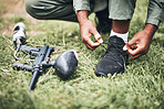 Paintball, gun and shooter or man kneeling ready for competitive match or competition in the forest. Player, athlete and person tying laces with game equipment or weapon on a sports field 