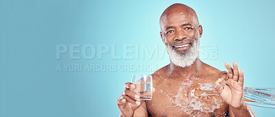 Buy stock photo Water splash, portrait and senior man in a studio with a glass of aqua and a ok hand gesture. Health, wellness and happy elderly African male with sign language by a blue background with mockup space