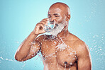 Drinking water, splash and skincare of black man in studio isolated on blue background. Wellness, cleaning and senior male model drink liquid for hydration, bathing and washing for health and hygiene