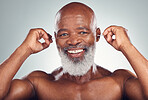 Portrait of black man cleaning ear with smile, body care and grooming isolated on grey background. Morning routine, health and happy senior male with earbuds in ears to clean for wellness in studio.