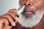 Black man, grooming and nose hair removal with an electric trimmer for shave, beauty and skin care. Face of African person with tools for nasal hygiene, facial routine or maintenance grey background