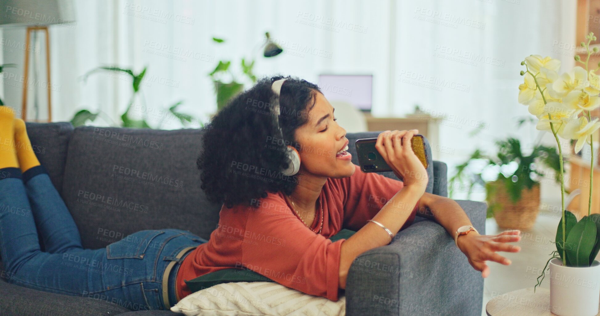 Buy stock photo Woman on sofa with earphones, phone and singing in living room, relax with streaming radio service. Music, energy and girl on couch in home listening to audio with internet, technology and headphones