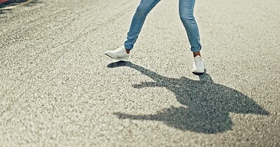 Feet, dancing and woman in city street for celebration, achievement or happy success with shadow or silhouette on asphalt road. Energy, freedom and urban hip hop dancer student girl legs and sneakers