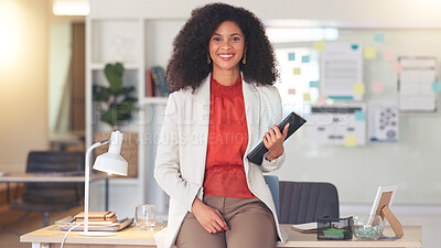 Young woman working on tablet and smiling. Young female is in an offie, sitting on a desk and busy working. She could be an accountant or lawyer speaking to a client or coworker.