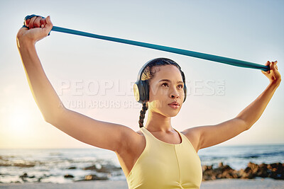 Buy stock photo Headphones, beach and woman with band stretching while streaming music, radio or podcast. Sunset, sports and female training with resistance band for health, fitness and wellness outdoors by ocean.