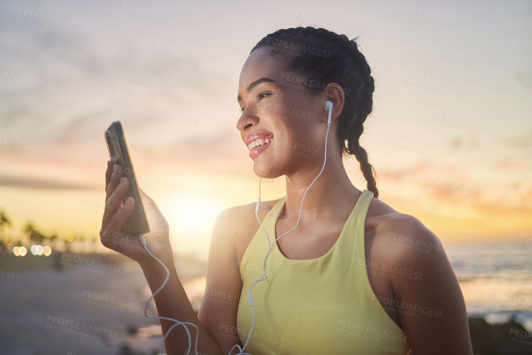 Buy stock photo Fitness, beach and woman with smartphone after running at sunset, online and streaming music or podcast in nature for exercise. Runner, relax and scroll social media after run, smile with earphones.