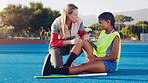 Women, hockey coach and knee injury girl on field together with support, solidarity or care at sport training. Sports woman, coaching or help at workout for joint pain at outdoor exercise with mentor