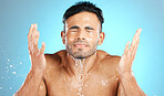 Water splash, face and man in studio for skincare, wellness and grooming on blue background. Cleaning, beauty and facial by Mexican model relax with luxury, routine and moisture while isolated