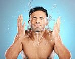 Facial, water splash and man in studio for skincare, wellness or grooming on blue background. Cleaning, beauty and moisture by Mexican model relax for luxury, routine or face treatment while isolated