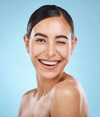 Buy stock photo Portrait, wink and skincare with a model woman in studio on a blue background for natural beauty. Face, skin and winking with an attractive young female posing to promote a luxury cosmetic product