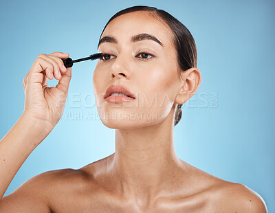 Buy stock photo Mascara, application and woman with makeup on face isolated on a blue background in a studio. Beauty, glam and model with cosmetics from a brush on an eyelash for facial treatment on a backdrop