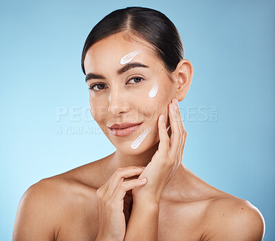 Buy stock photo Portrait, beauty and cream with a woman in studio to apply treatment on a blue background for skincare. Face, skin and lotion with an attractive young female posing to promote a luxury product