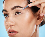 Hair removal, tweezer and woman doing her eyebrows in studio for beauty, facial and grooming routine. Cosmetics, depilation and female model plucking face hair with cosmetic tool by blue background.