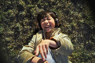 Buy stock photo Headphones, nature and Asian child on the grass to relax, chill and listen to music with freedom. Happy, smile and excited girl kid streaming a podcast or the radio in outdoor field, park or garden.