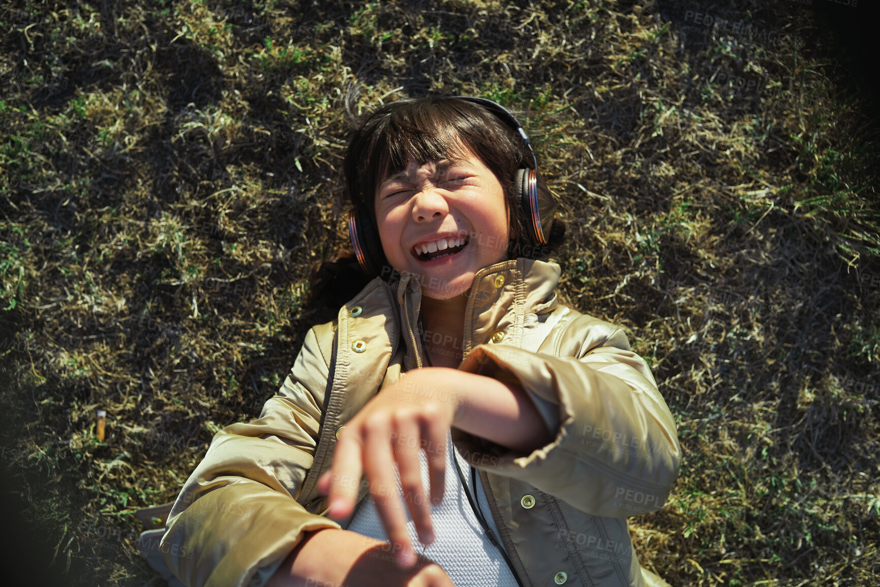 Buy stock photo Headphones, nature and Asian child on the grass to relax, chill and listen to music with freedom. Happy, smile and excited girl kid streaming a podcast or the radio in outdoor field, park or garden.