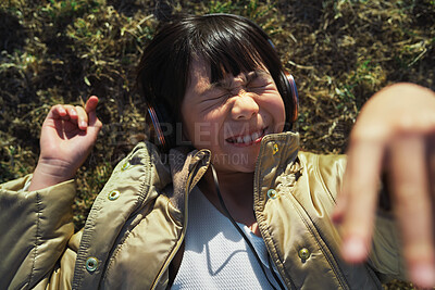Buy stock photo Funny, playful and girl with headphones on grass for freedom, comedy and crazy in Singapore. Summer, comic and Asian child lying in park to relax, streaming music and lisrening to audio while playing